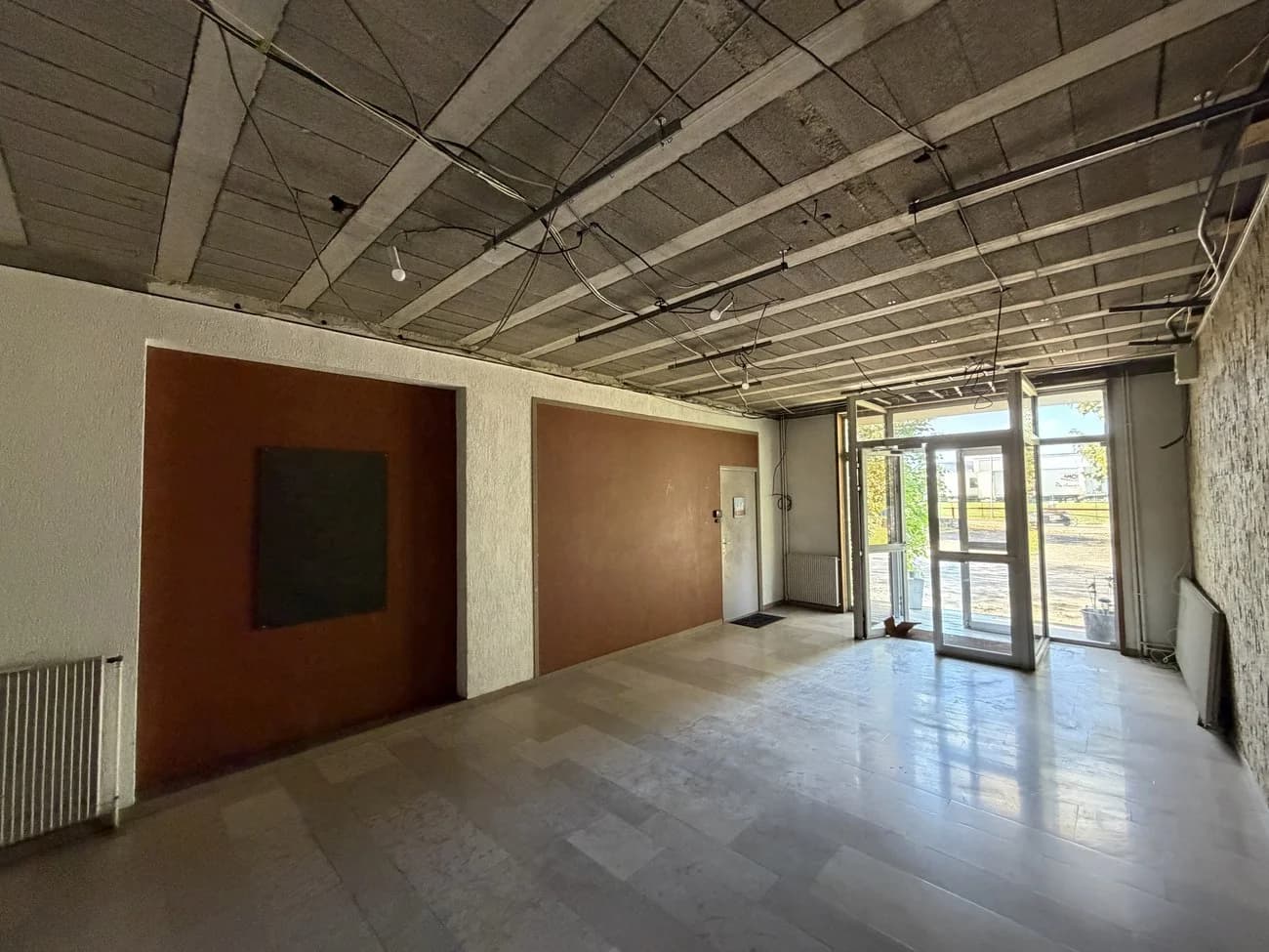 Hall d’immeuble en cours de rénovation avec accès vitré, sol carrelé et plafond ouvert